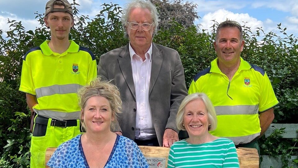 People sitting on and standing around the Happy to chat bench